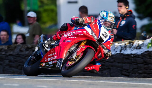 Motorcycle racer in red racing suit leaning into a turn on a red sport bike with number 3, during a race.