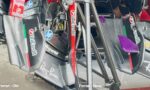 Close-up of Ferrari F1 front wing components with carbon fiber panels and sponsor logos, showing old vs. new versions labeled at the bottom left and right.
