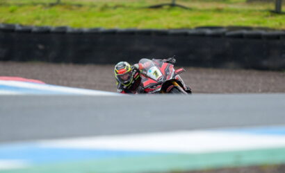 Motorcyclist in a racing suit leaning into a turn on a race track, red and black bike with number plate 7