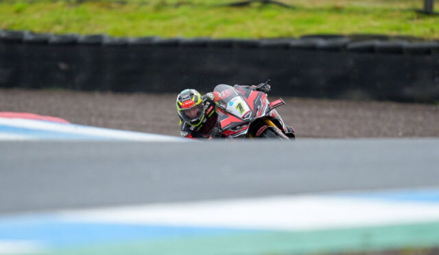 Motorcyclist in a racing suit leaning into a turn on a race track, red and black bike with number plate 7