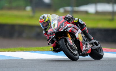 MotoGP rider leaning into a sharp turn on a red-and-white race bike, number 1, on a wet track.