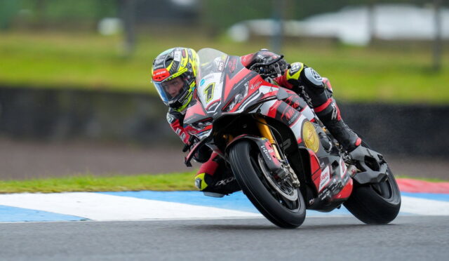 MotoGP rider leaning into a sharp turn on a red-and-white race bike, number 1, on a wet track.