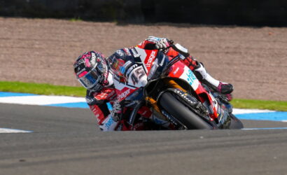 Motorcycle racer leaning into a sharp turn on a race track.