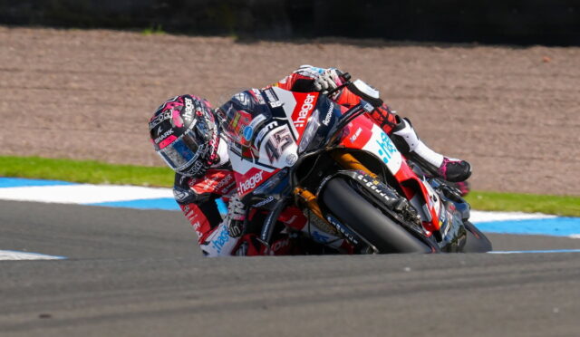 Motorcycle racer leaning into a sharp turn on a race track.