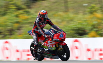 Motocycle racer in red and black suit riding a red sport bike at speed on a race track, number 4 visible on the bike.