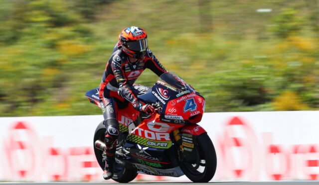 Motocycle racer in red and black suit riding a red sport bike at speed on a race track, number 4 visible on the bike.