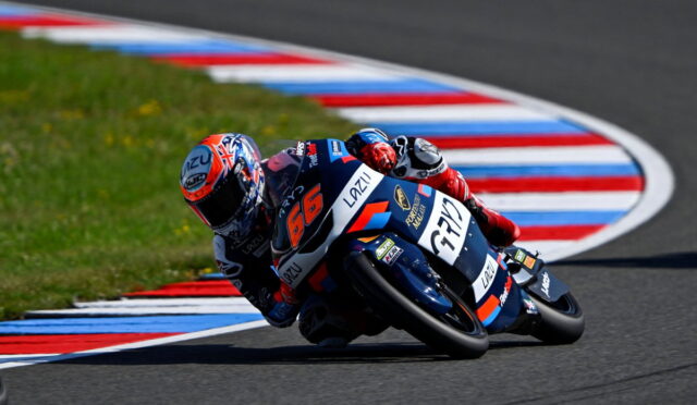 Two motorcycle racers leaning into a curve on a racetrack, bike number 56 in blue and orange fronting the pair.
