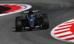 Mercedes Formula 1 car navigates a sharp left turn on a race track, hugging the red-and-white curbs at speed.