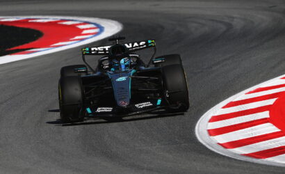 Mercedes Formula 1 car navigates a sharp left turn on a race track, hugging the red-and-white curbs at speed.