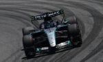 Mercedes Formula 1 car from Petronas cornering hard on a race track, tires smoking slightly on a left-hand turn.