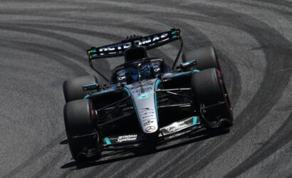 Mercedes Formula 1 car from Petronas cornering hard on a race track, tires smoking slightly on a left-hand turn.