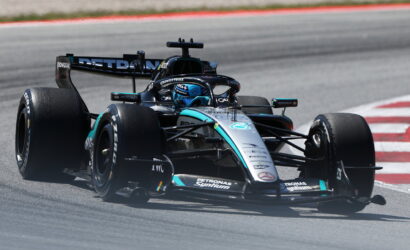 Mercedes‑AMG Petronas F1 car taking a turn on a race track with red and white curbs nearby.