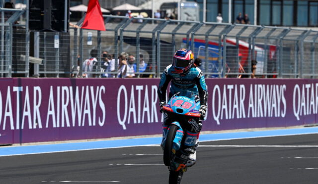 Motorcycle racer performing a wheelie on a race track, rider in turquoise suit with #23, Qatar Airways banners in the background
