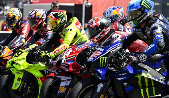 Group of motorcycle racers leaning into a tight start on a race track, colorful bikes and helmets close together.