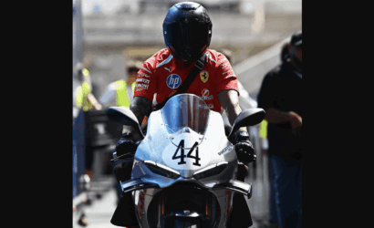 Racing rider in red team suit on a white Ducati motorcycle numbered 44, wearing a black helmet in the pit area.