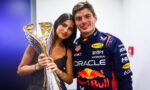 Race car driver in a blue Red Bull Honda suit posing with a tall golden trophy beside a smiling woman.