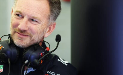 Close-up of a smiling man wearing a black racing headset with a microphone in front of him