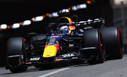 Formula 1 car racing on a track with blue and yellow Red Bull livery and sponsor decals visible on the nose and wings, speeding through a corner.