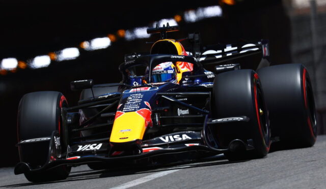 Formula 1 car racing on a track with blue and yellow Red Bull livery and sponsor decals visible on the nose and wings, speeding through a corner.