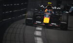 Red Bull Racing Formula 1 car speeding along a track beside barriers, driver in helmet visible.