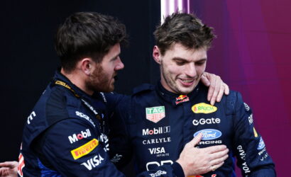 Two race car drivers in blue sponsor suits share a congratulatory hug on stage.
