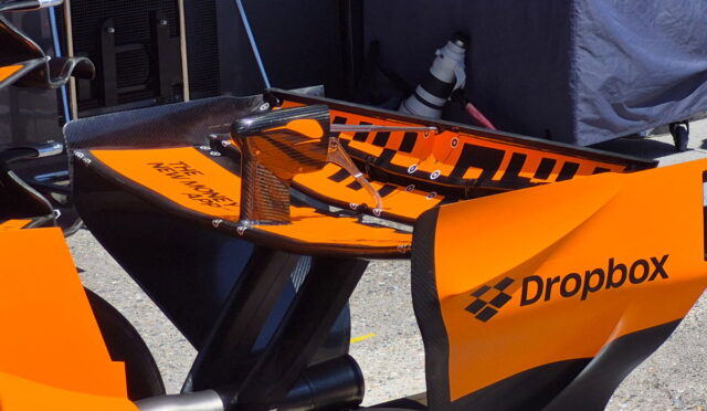 Orange race bike with carbon fiber components on a stand in a pit area, Dropbox branding on the side panel.
