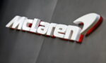 McLaren logo in white lettering with a subtle red shadow on a dark gray wall