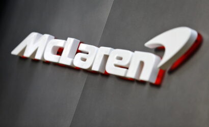 McLaren logo in white lettering with a subtle red shadow on a dark gray wall