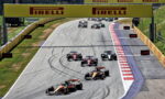 Formula 1 race on a curving track with several race cars close together under a large Pirelli sign.