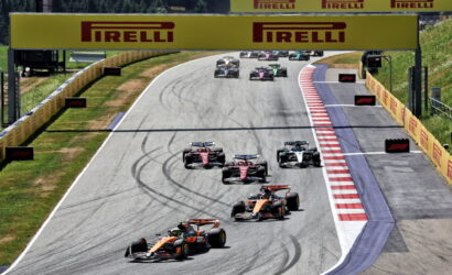 Formula 1 race on a curving track with several race cars close together under a large Pirelli sign.