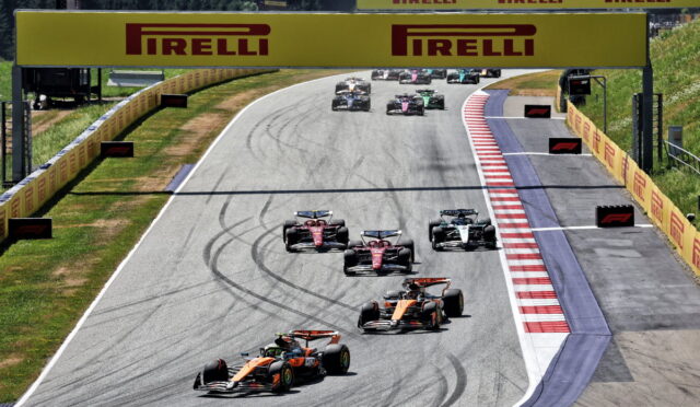 Formula 1 race on a curving track with several race cars close together under a large Pirelli sign.