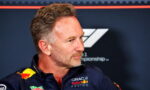 Side-profile of a man with short gray hair and stubble, wearing a navy Red Bull Racing polo at a press event.