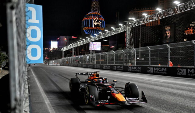 Nighttime Formula 1 car speeds along a barrier-lined Las Vegas street circuit, with bright lights and MGM Rewards banners along the track.