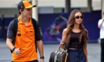 Young man in an orange polo and cap gives a thumbs up while walking beside a woman with sunglasses and a designer LV handbag outside.