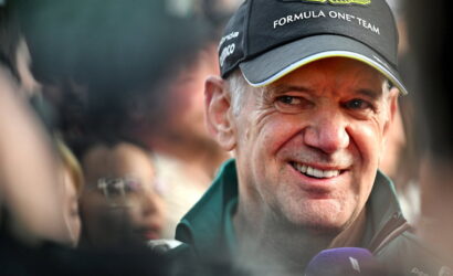 Smiling man wearing an Aston Martin Formula One cap, surrounded by fans.