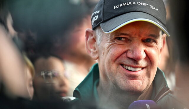 Smiling man wearing an Aston Martin Formula One cap, surrounded by fans.