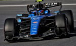 Blue open-wheel Formula 1 race car on a track, driver in helmet visible in the cockpit, front wing and aero complex in focus for a dynamic speed shot