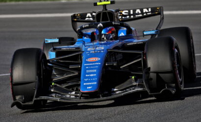 Blue open-wheel Formula 1 race car on a track, driver in helmet visible in the cockpit, front wing and aero complex in focus for a dynamic speed shot
