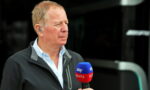 Side-profile of an older man in a light blue shirt and dark jacket, holding a blue and red Sky Sports microphone during an interview.