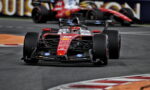 Red Ferrari Formula 1 car rounding a corner on a race track with another car blurred in the background.