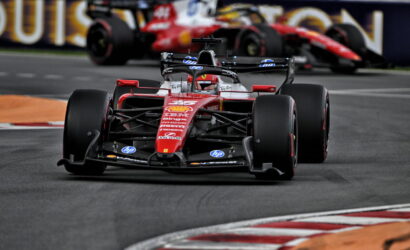 Red Ferrari Formula 1 car rounding a corner on a race track with another car blurred in the background.