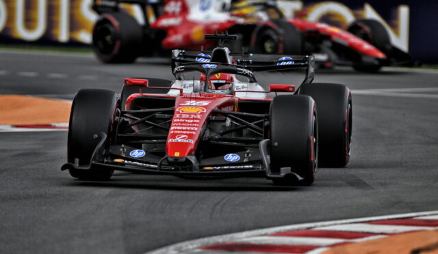 Red Ferrari Formula 1 car rounding a corner on a race track with another car blurred in the background.