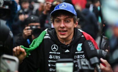 Young man in a blue Mercedes cap being interviewed by reporters with cameras around him.