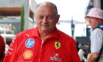 Smiling man in a red Ferrari team polo with sponsor logos (HP, Shell, UniCredit) outdoors in a paddock area.