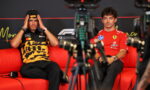 Two Formula 1 drivers sit on a red couch for an interview, cameras in the foreground.
