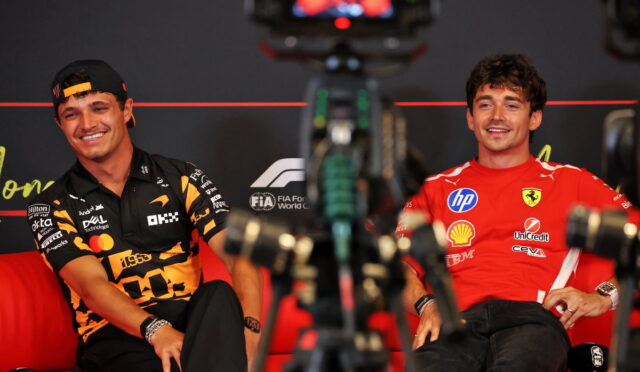 Two Formula 1 drivers sit on a red sofa during an interview, smiling, with camera gear in the foreground.