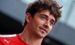 Portrait of a young man with tousled brown hair wearing a red sports jersey, looking slightly to the side, with a blurred background.