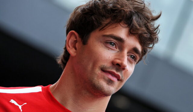 Portrait of a young man with tousled brown hair wearing a red sports jersey, looking slightly to the side, with a blurred background.