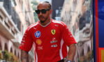 Man wearing a red Ferrari polo with sponsor logos, sunglasses, and chain walks down a city street.