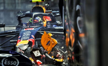 Close-up of a Red Bull Formula 1 car in a crash, with a damaged front wing and debris flying near the cockpit.
